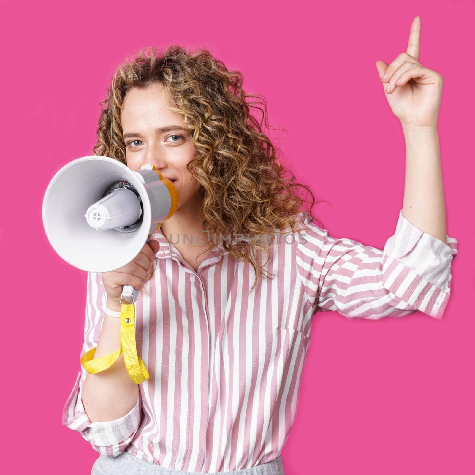 Young woman speaks into a megaphone and raises her finger up. Isolated pink background. by Sd28DimoN_1976