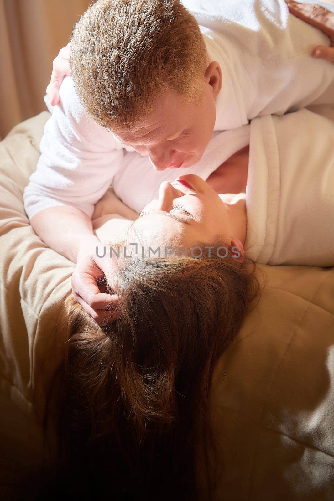 An adult couple of newlyweds in in white robes in a hotel room after the wedding. A guy and a girl, a man and a woman in beautiful room. The concept of hugs, love and care