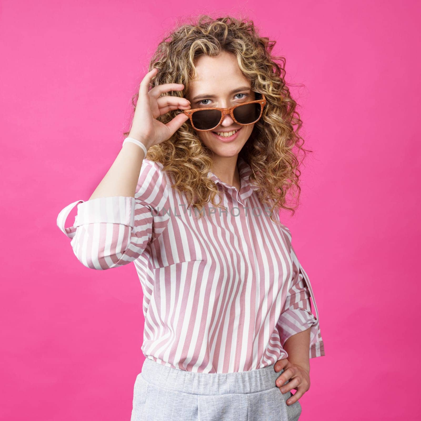 Portrait of a young, beautiful, healthy woman holding glasses and looking at the camera. Isolated on pink background.