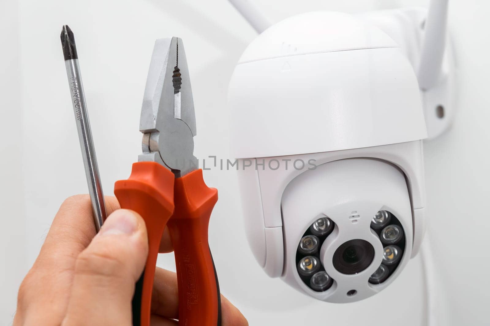 Technician installing CCTV camera using pliers and screwdriver outside of the building.
