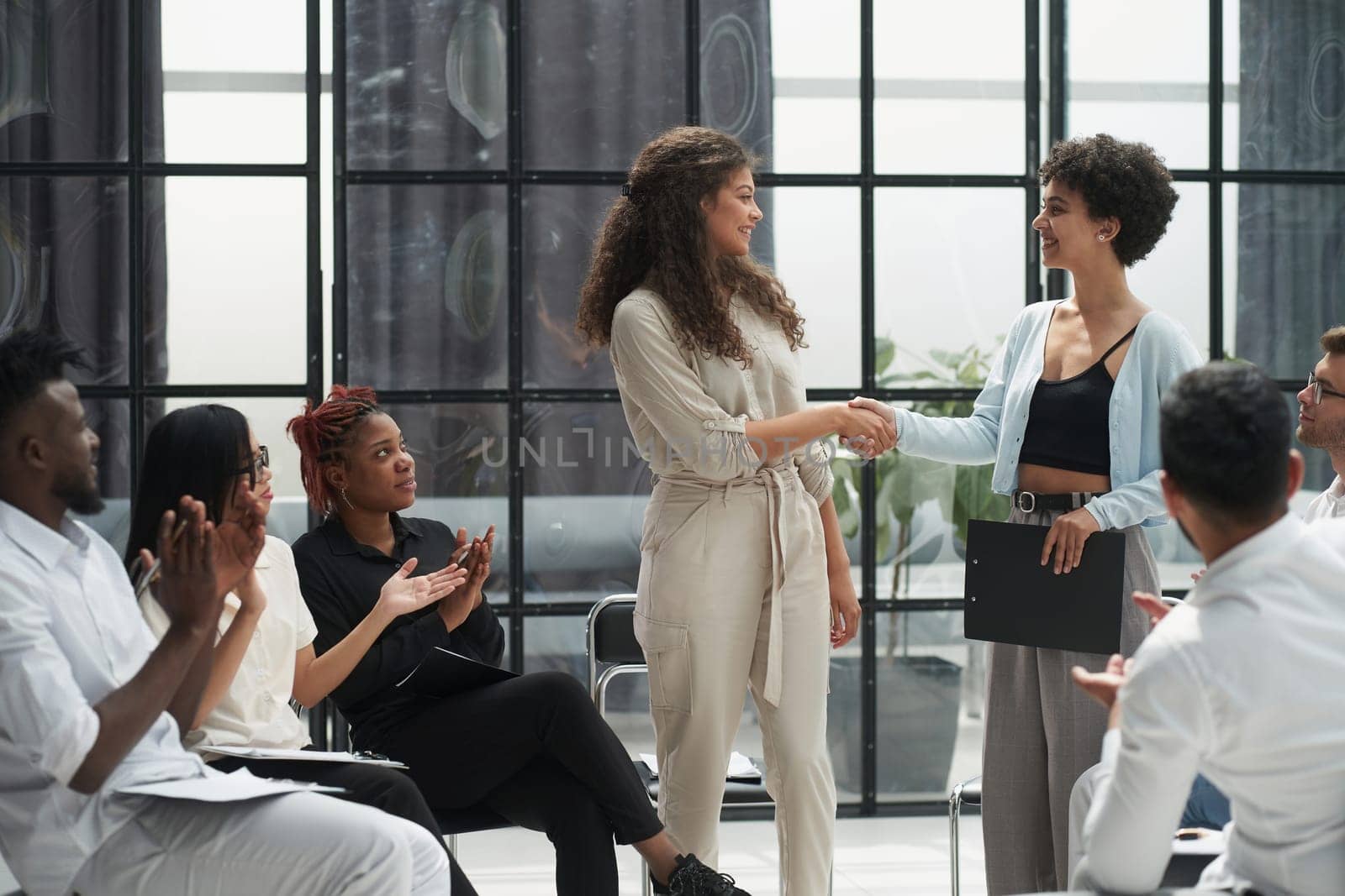 Welcome aboard. Group of business people sitting on a chair while two people shake hands by Prosto