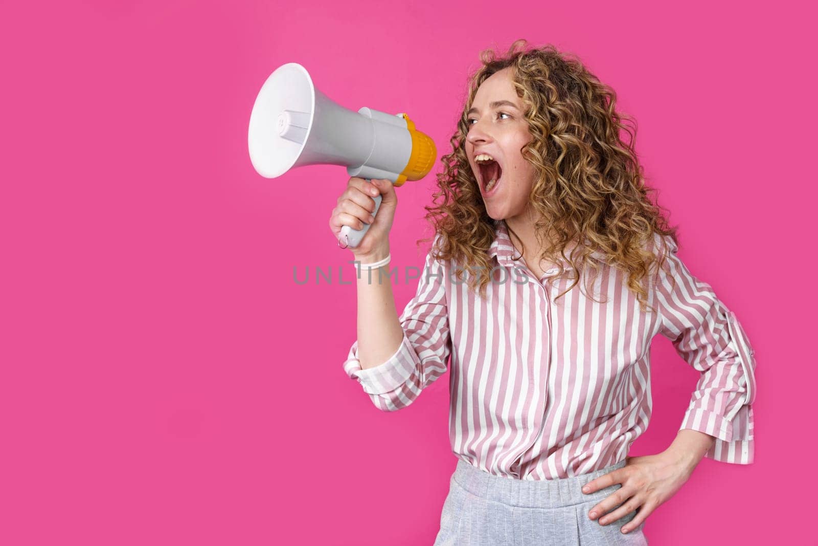 Young woman shouts into a megaphone. Isolated pink background. People sincere emotions lifestyle concept.