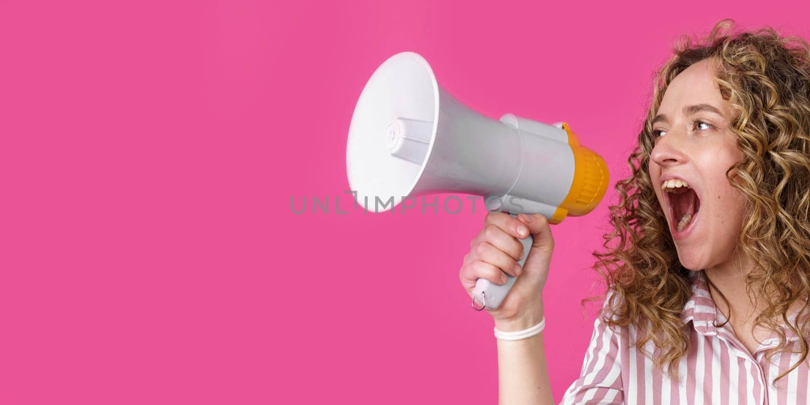 Young woman shouts into a megaphone. Isolated pink background. People sincere emotions lifestyle concept.