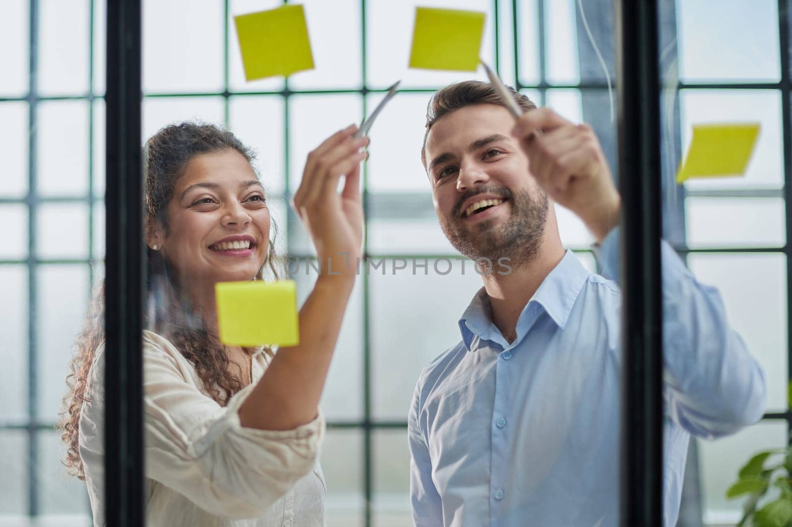 Creative professionals standing and discussing in office behind glass wall with sticky notes