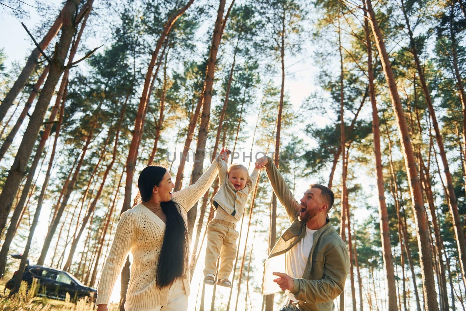 Holding little girl by hands. Happy family of father, mother and little daughter is in the forest.