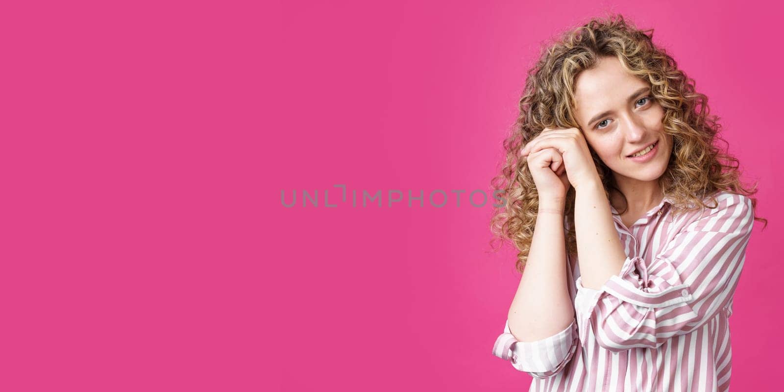 Happy contented woman holds her hands together near the face. Isolated on pink background