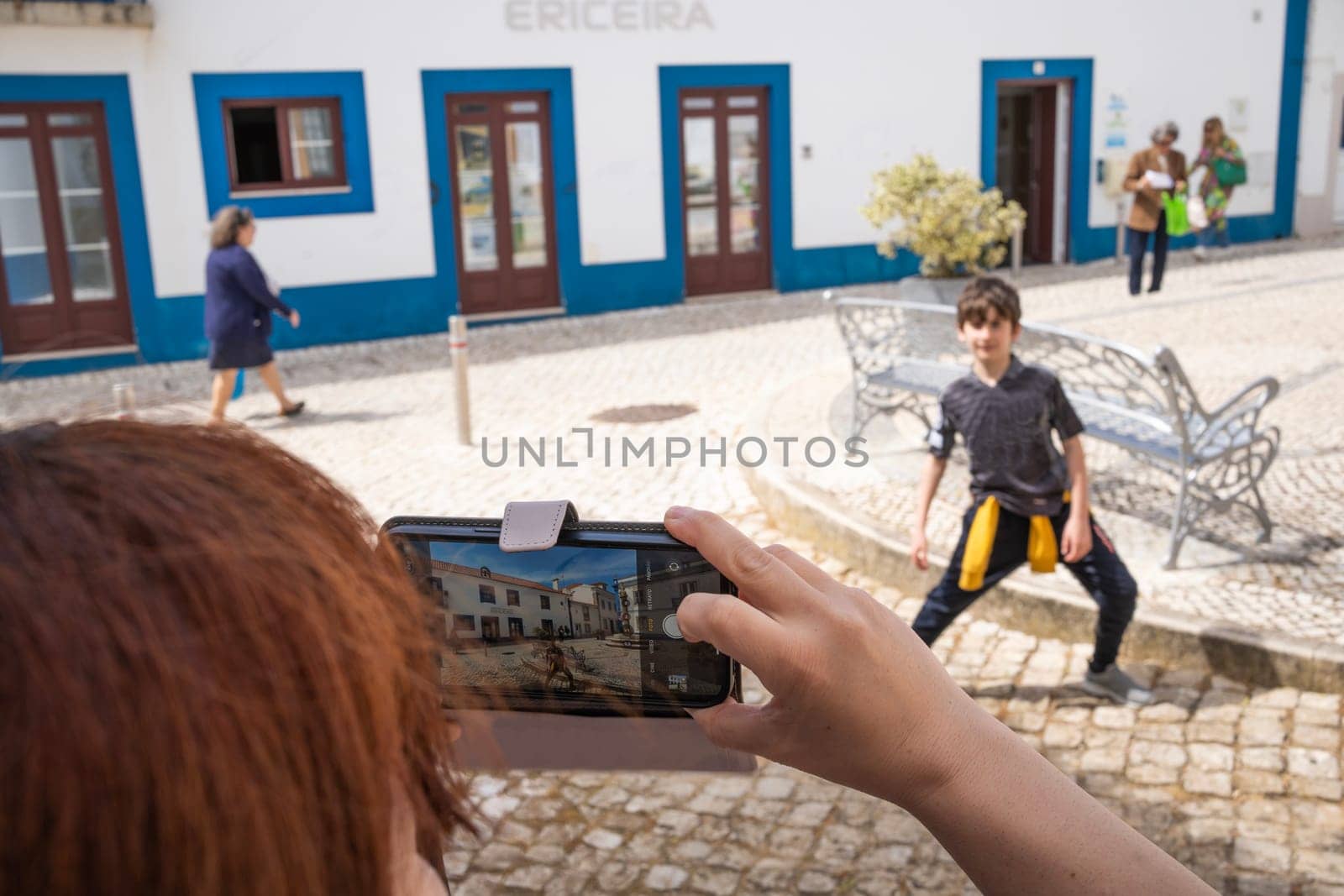 Mom taking mobile picture of her son in Ericeira downtown square , Portugal