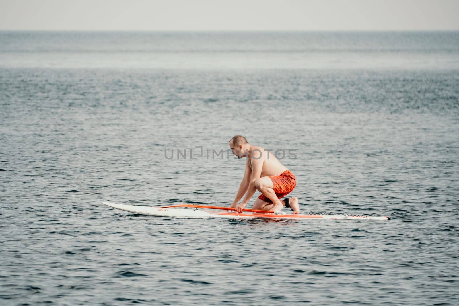 Active mature male paddler with his paddleboard and paddle on a sea at summer. Happy senior man stands with a SUP board. Stand up paddle boarding - outdor active recreation in nature