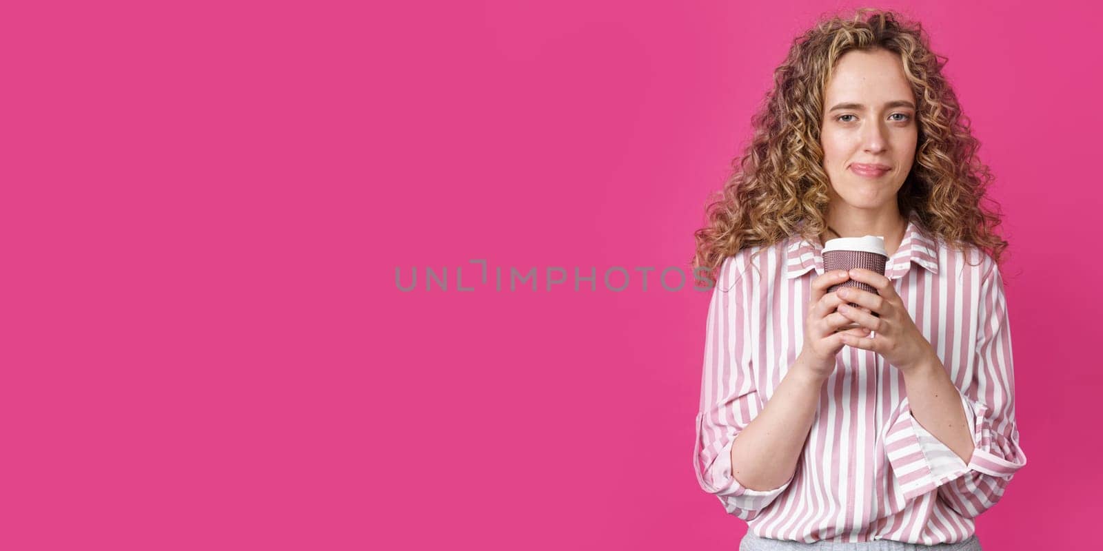 Young beautiful woman holding coffee in her hands. Isolated pink background