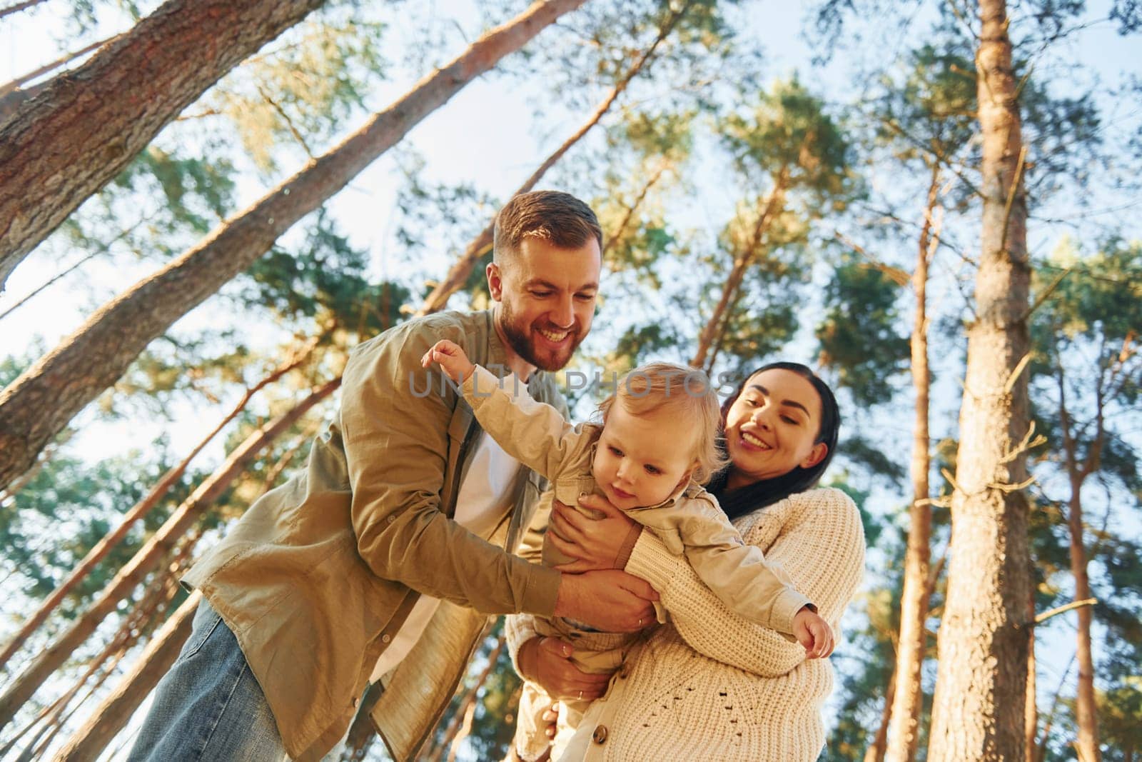 Holding little girl by hands. Happy family of father, mother and little daughter is in the forest.