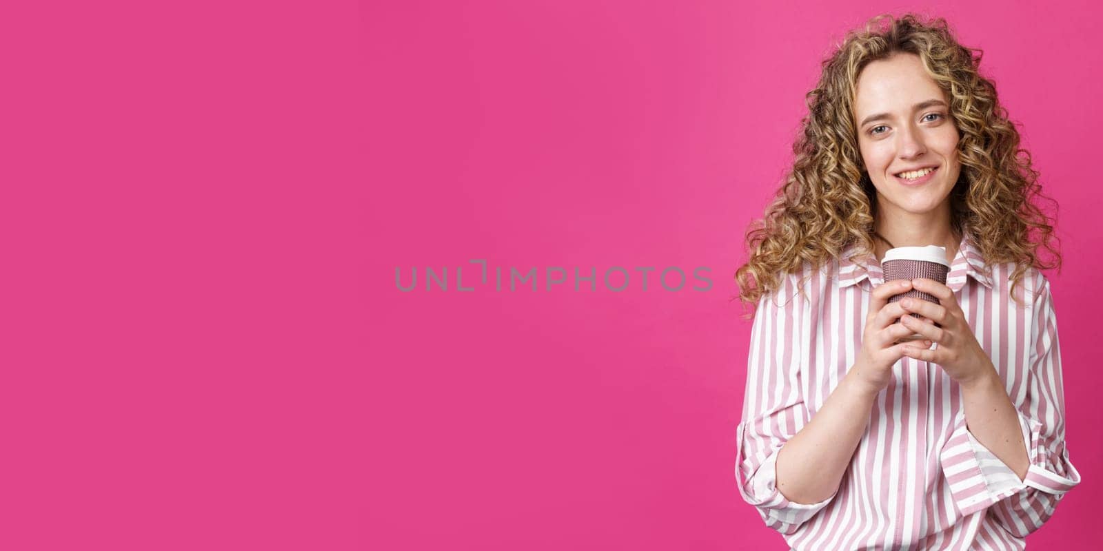 Young beautiful woman holding coffee in her hands and smiling. Isolated pink background