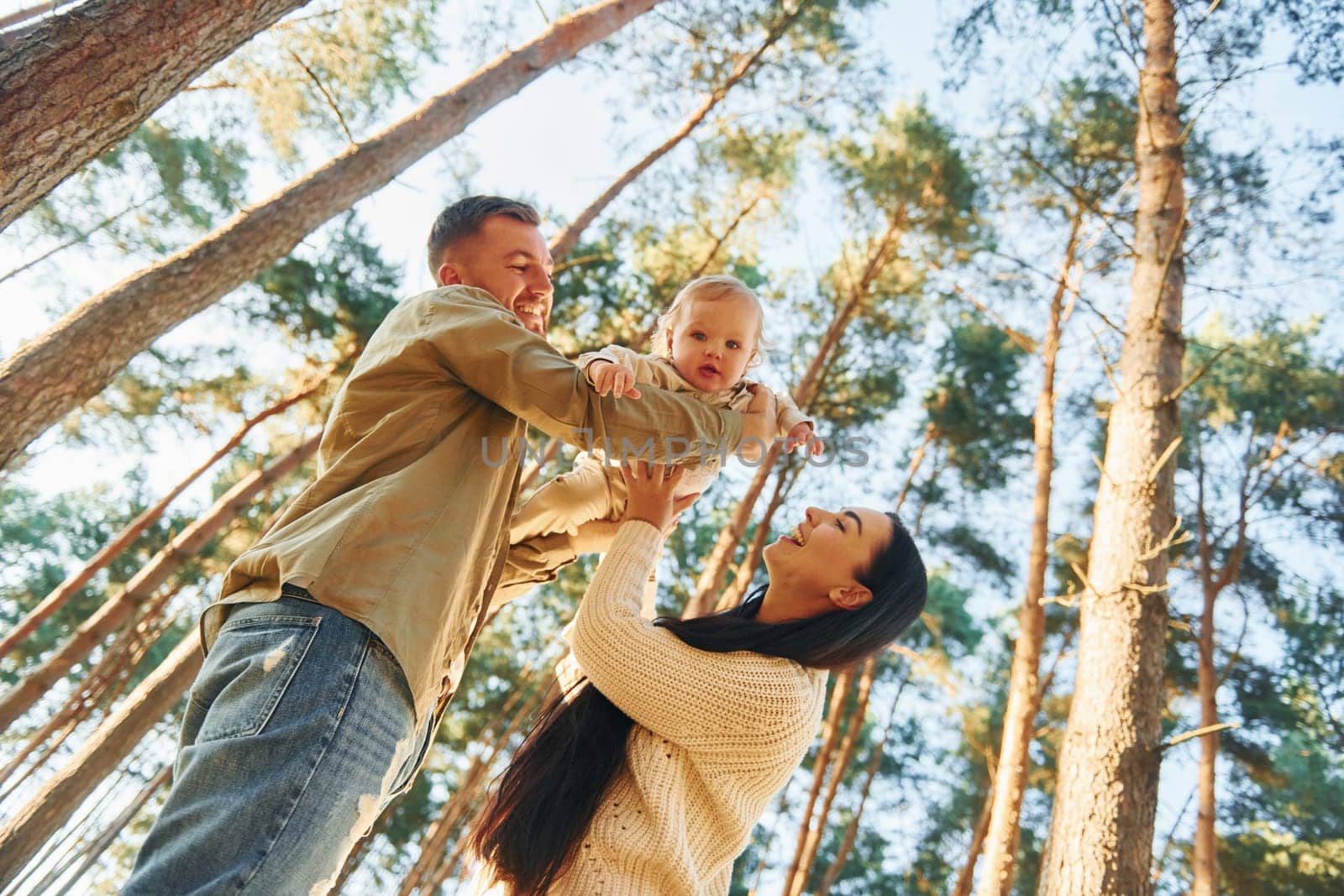 View from below. Happy family of father, mother and little daughter is in the forest by Standret