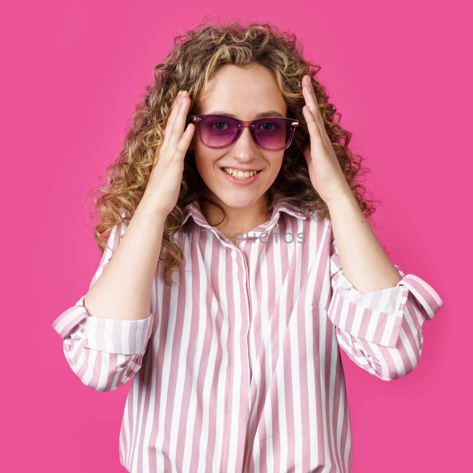 A young woman holds her head with her hands with delight and joy. Isolated on pink background