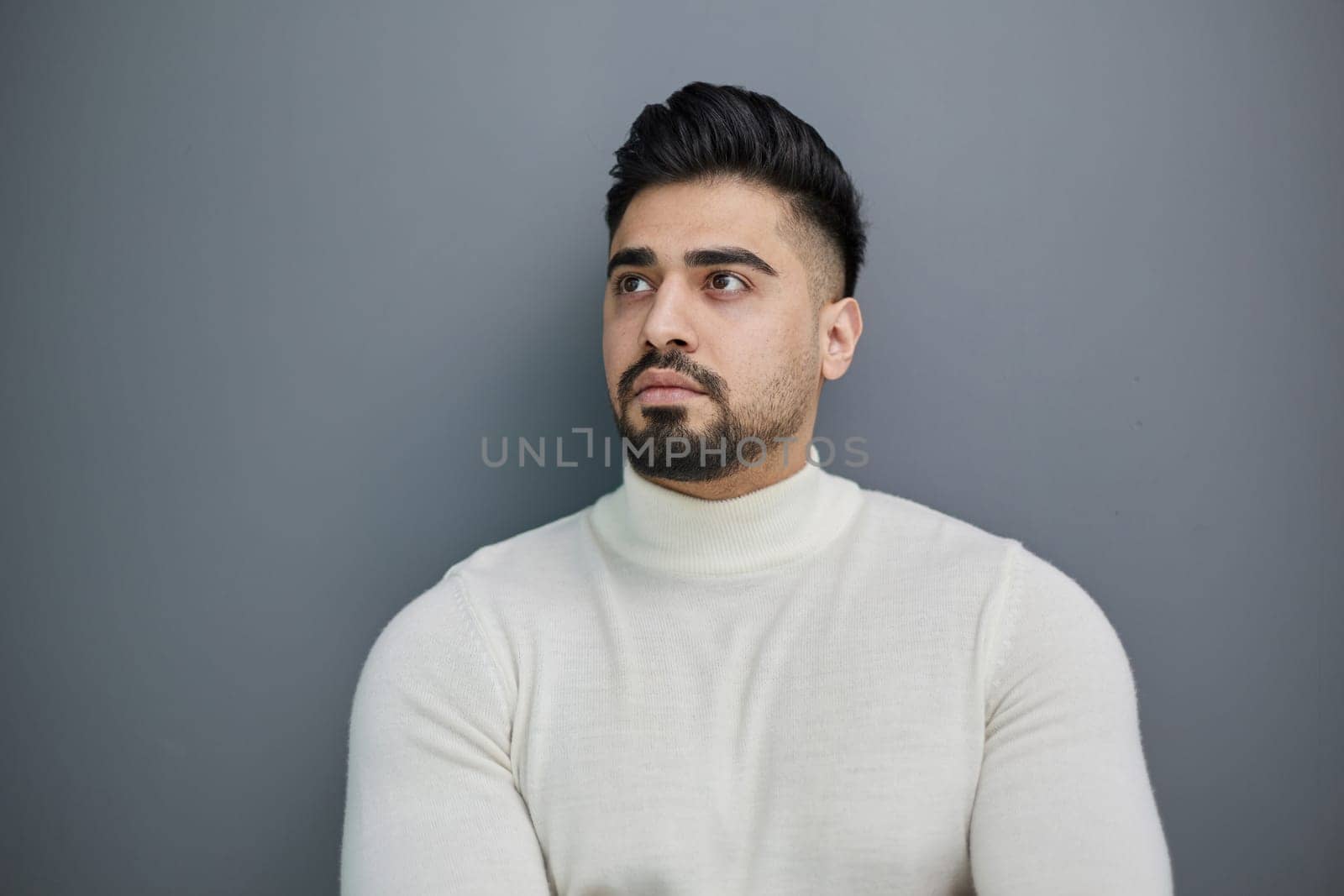Portrait of a stylish man posing on a gray background with his arms crossed
