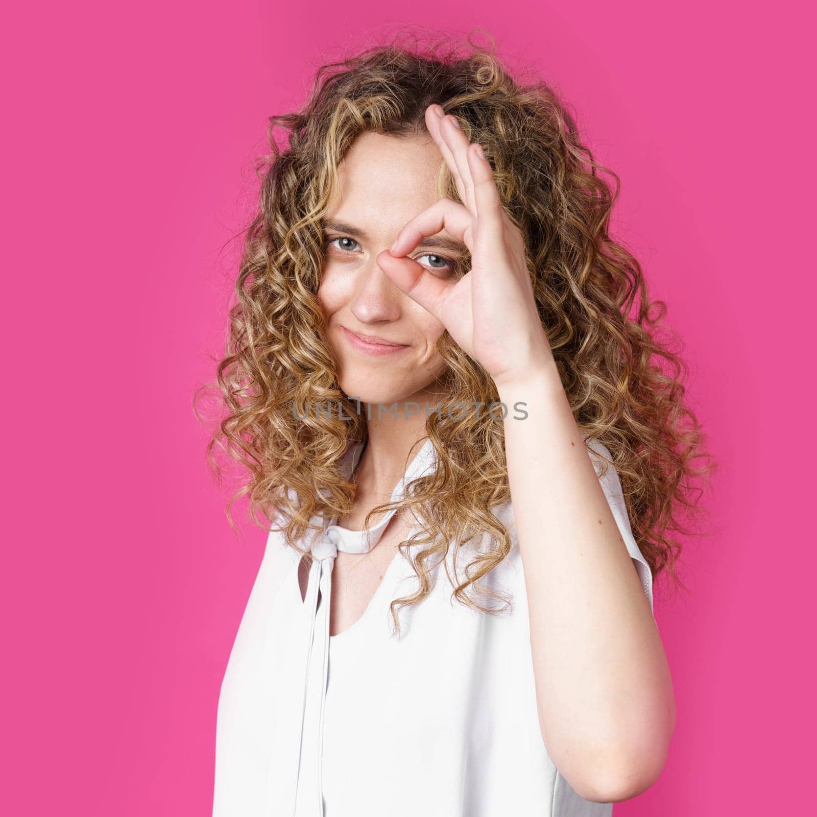 Portrait of a beautiful young woman makes a ok gesture, demonstrates agreement, loves an idea, smiles happily, models indoors. Well thank you. Hand sign