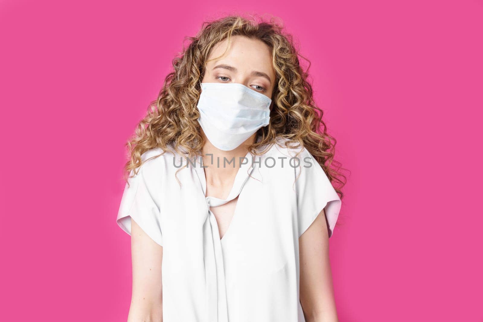 Young woman with a medical mask on her face shrugs. Isolated pink background