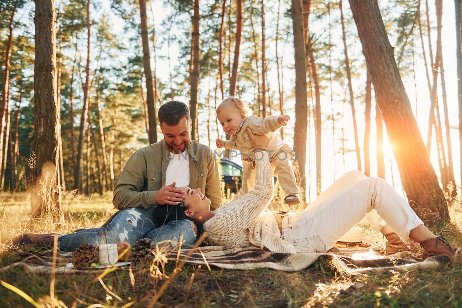 Woman is laying down. Happy family of father, mother and little daughter is in the forest.