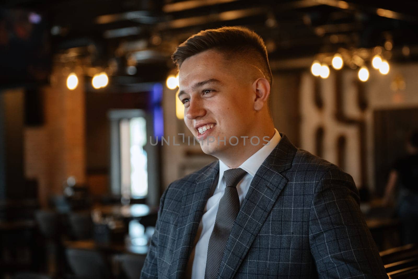 portrait of a groom in a gray plaid suit with a tie on the wedding day in a bar