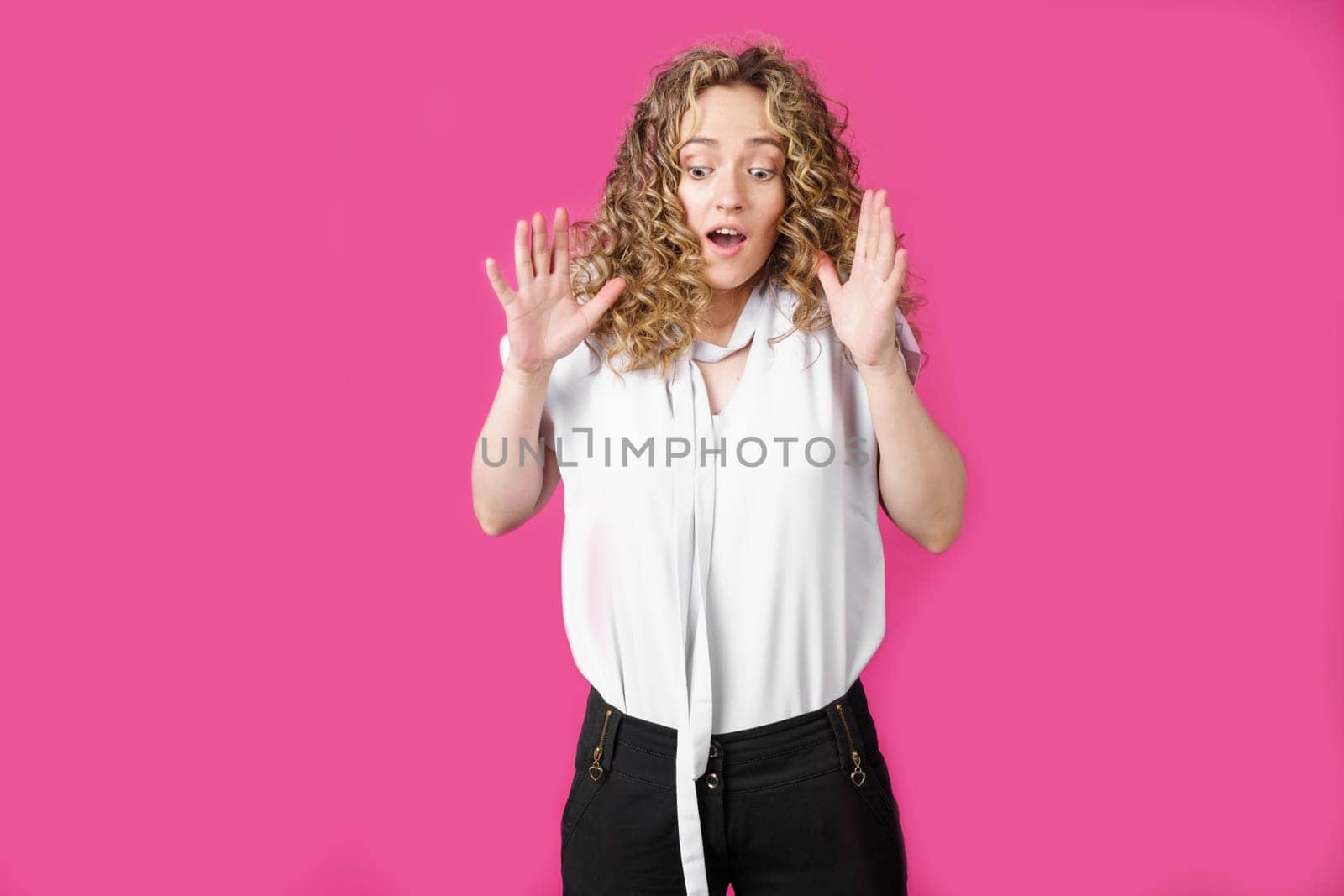 Young woman expressing emotions, raised her hands up. Female portrait. Isolated on pink background