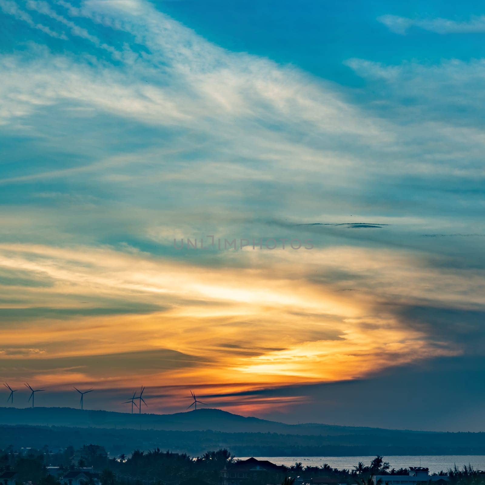 A sunset with a wind farm in the background colorful blue orange yellow bright.