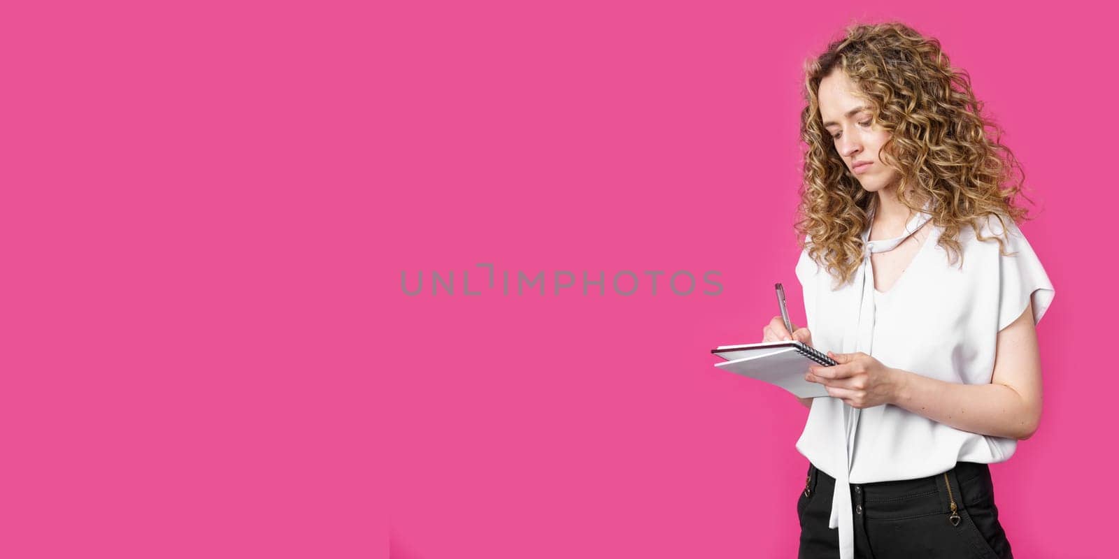 A charming woman makes entries in the diary. Isolated on a pink background.