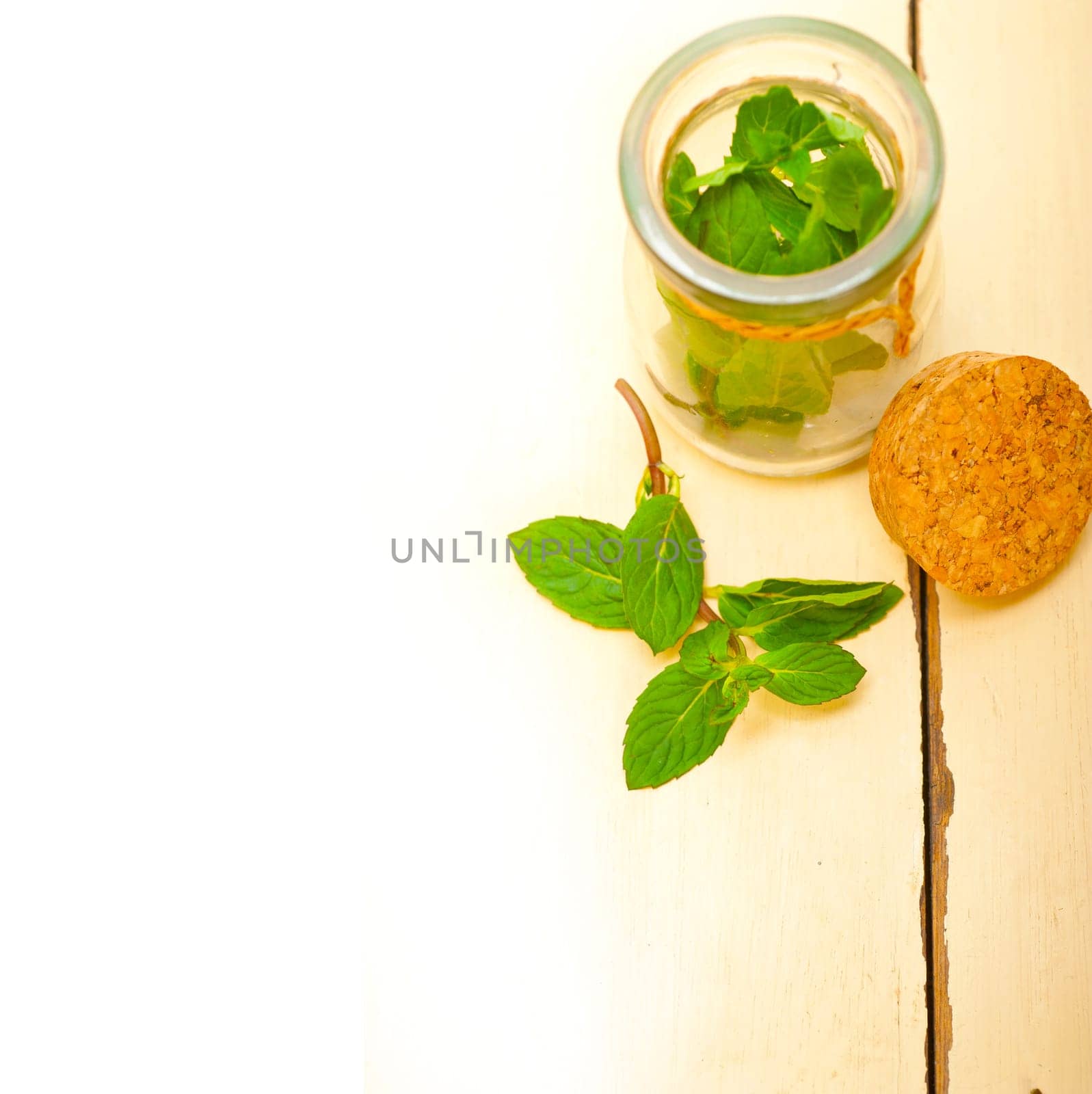 fresh mint leaves on a glass jarover a rustic white wood table