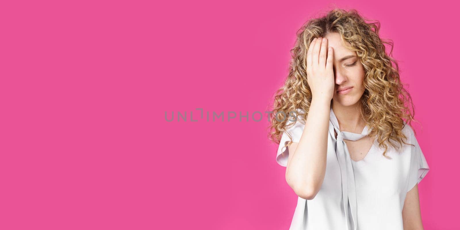 A young woman holds on to her sore head. Female portrait. Isolated on pink background
