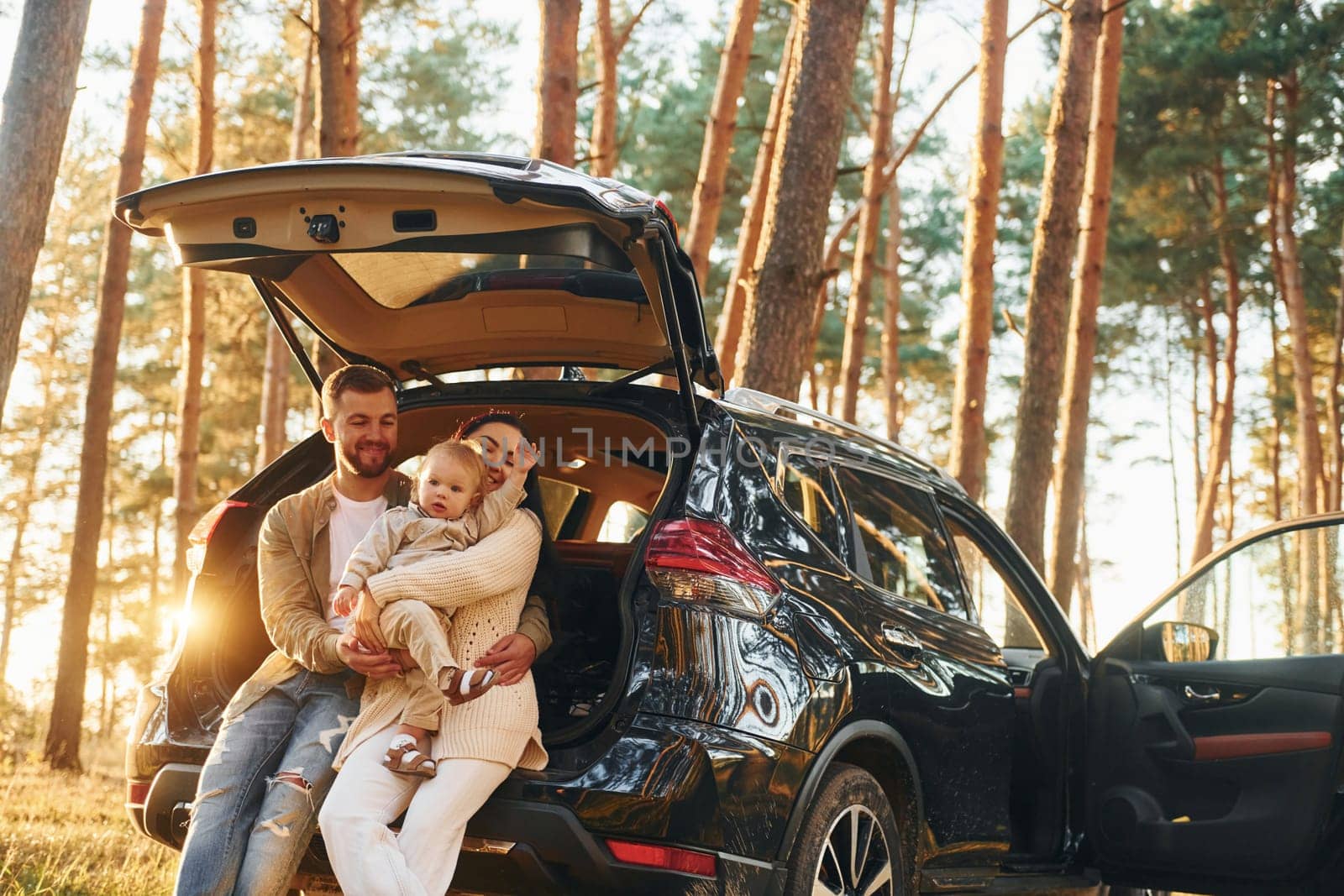 Leaning on the car. Happy family of father, mother and little daughter is in the forest.