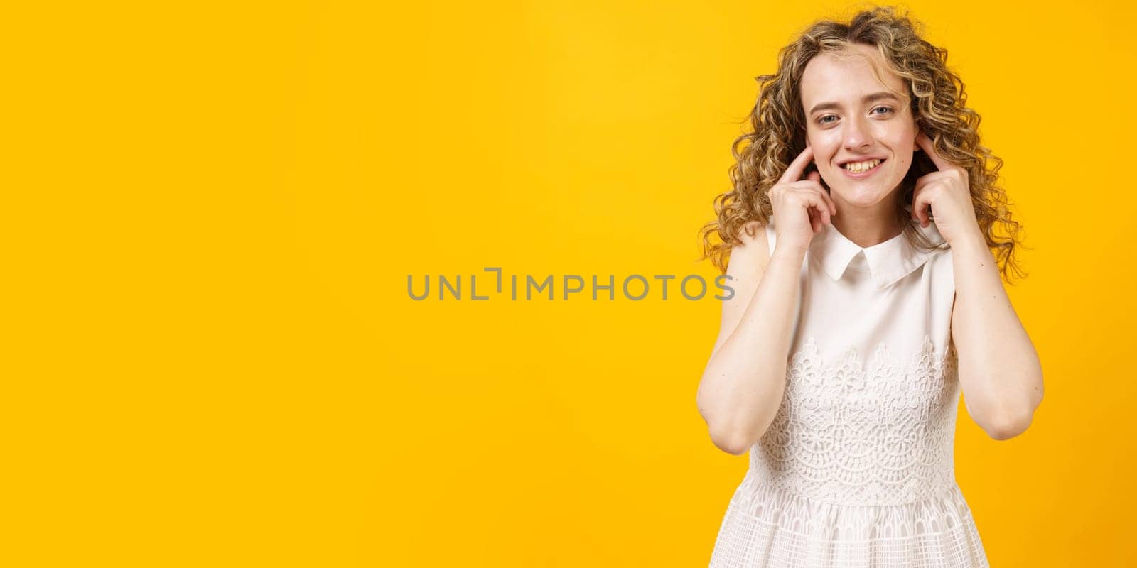 Portrait of a young woman who covered her ears with her fingers. Isolated on yellow background