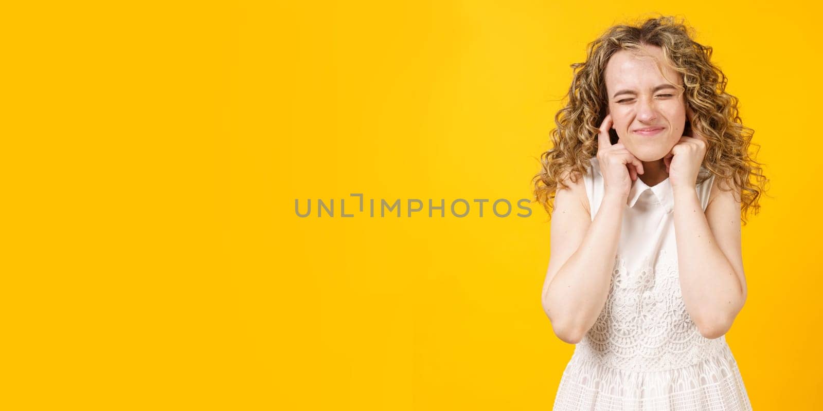 Portrait of a young woman who covered her ears with her fingers. Isolated on yellow background