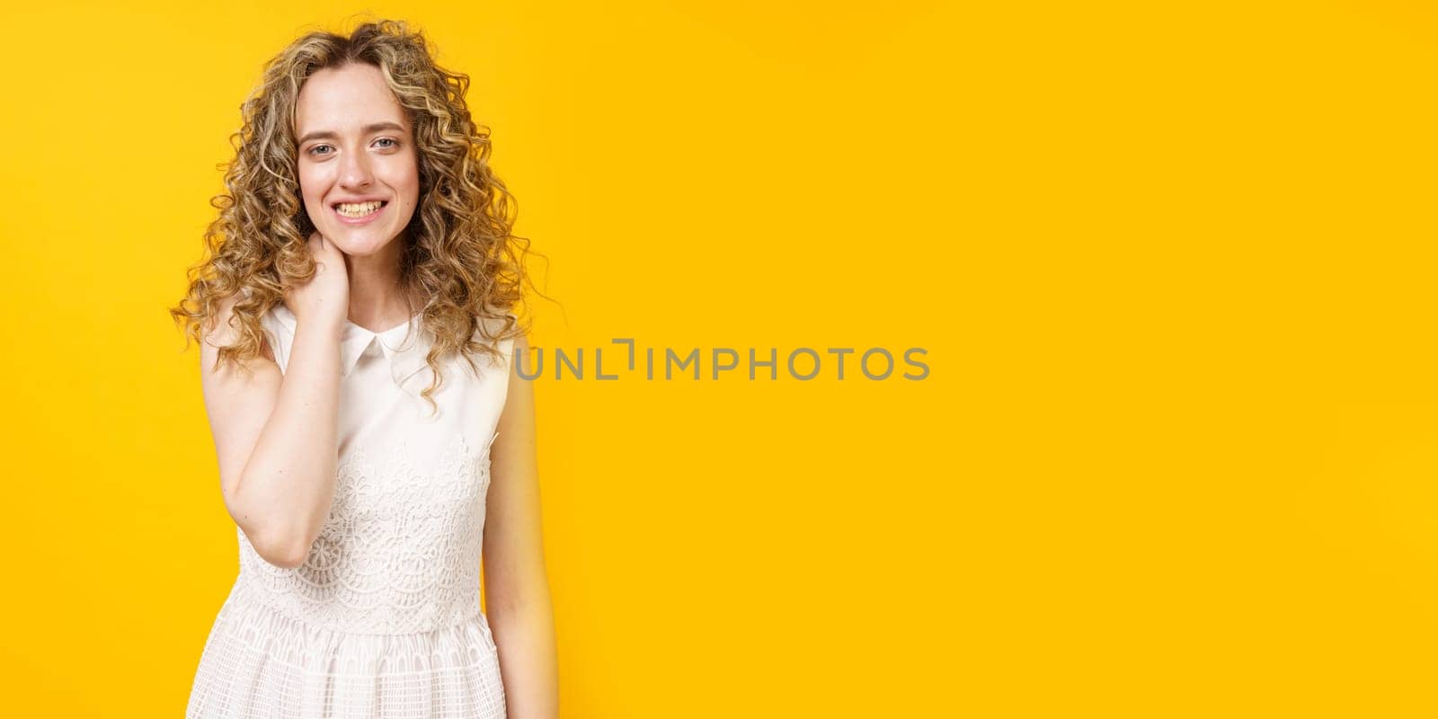 Portrait of a young smiling woman who holds her hand around her neck. Female portrait. Isolated on yellow background