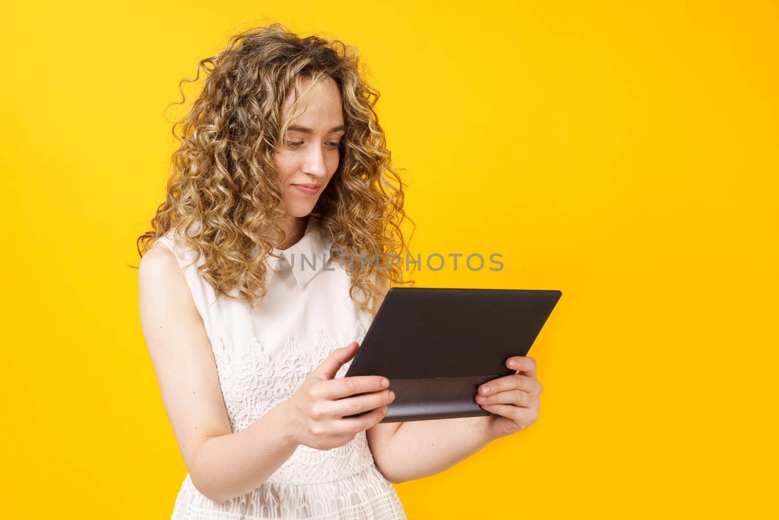 Portrait of a young woman who communicates on a tablet. Female portrait. Isolated on yellow background