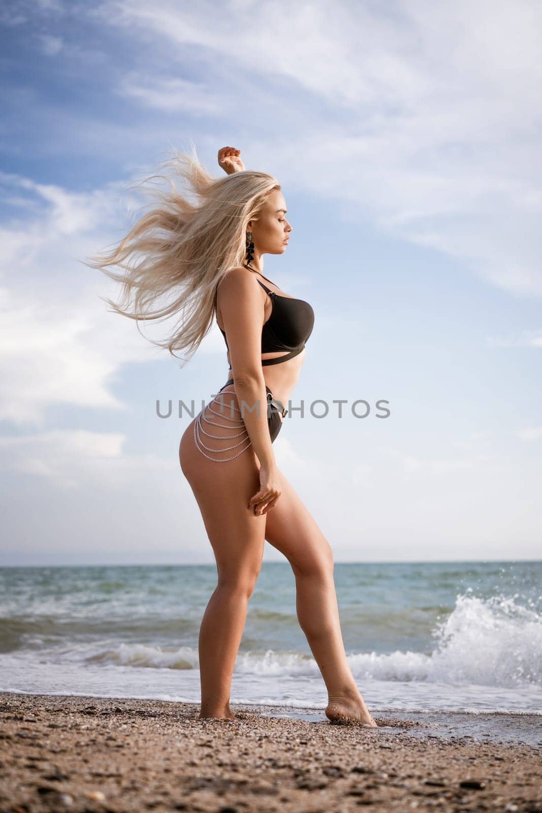 Slender woman posing while standing on the beach in a black swimsuit by EkaterinaPereslavtseva