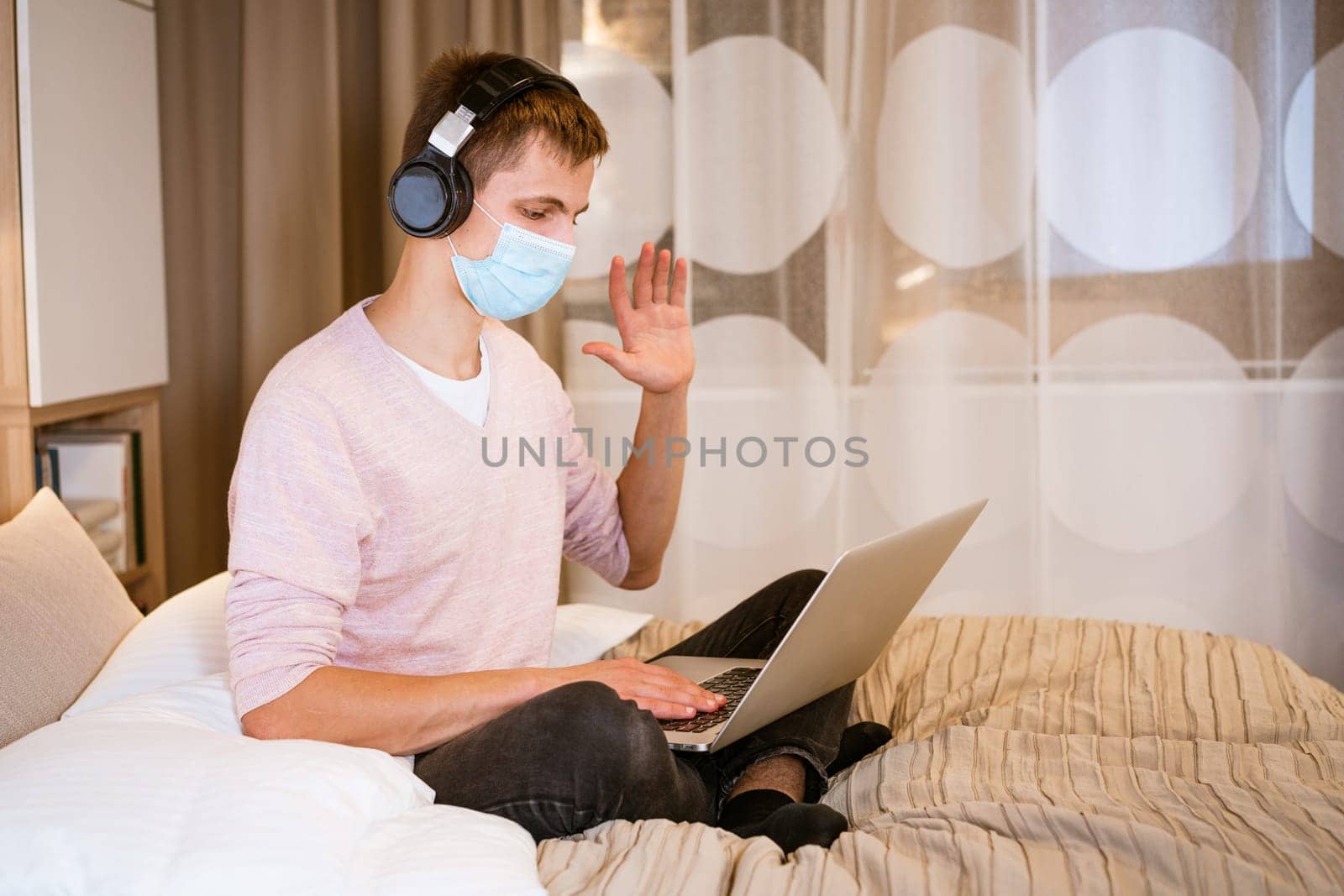 young man in headphones and protective mask at home with laptop by EkaterinaPereslavtseva