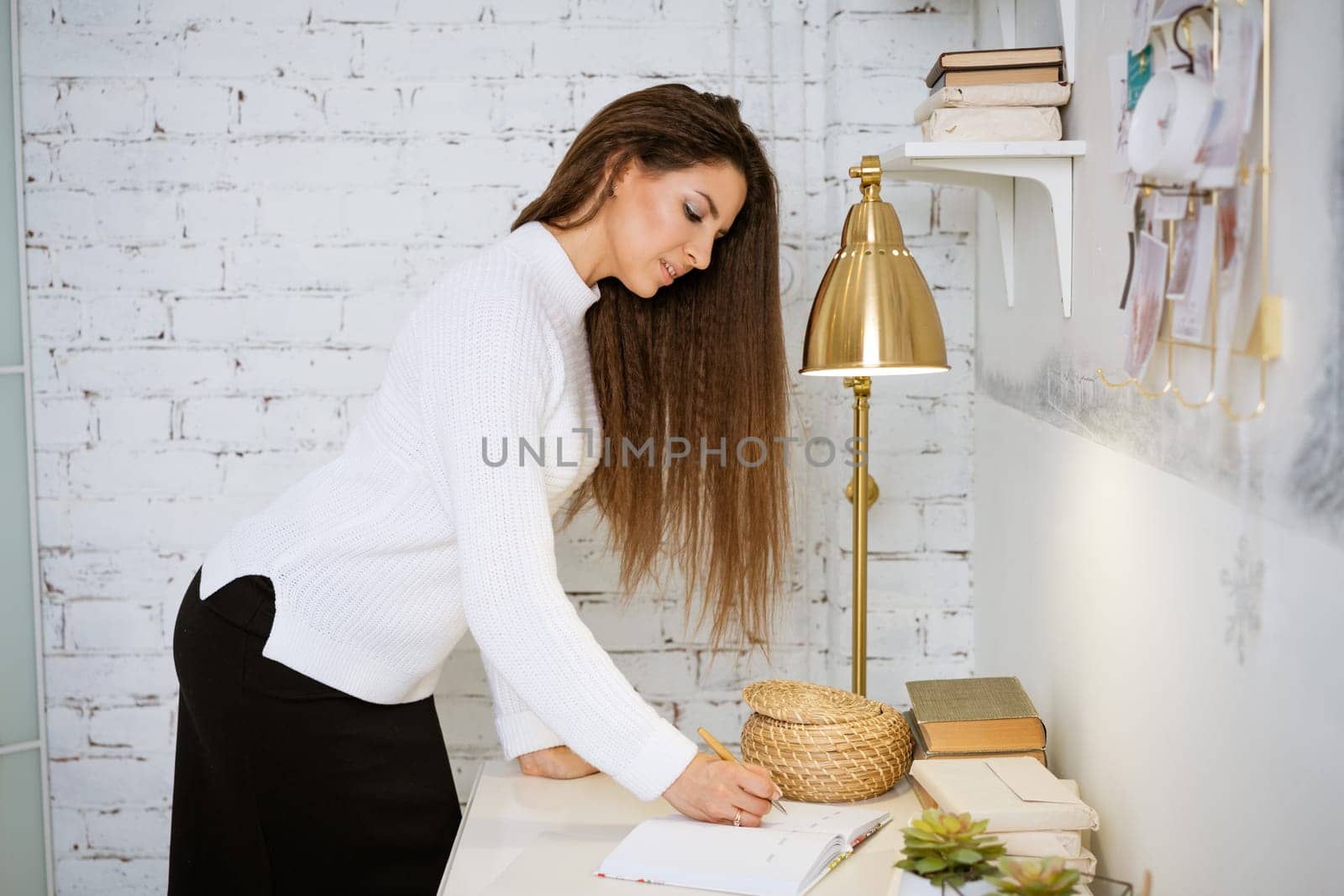 business woman in a white sweater writes in a notebook while sitting at the table