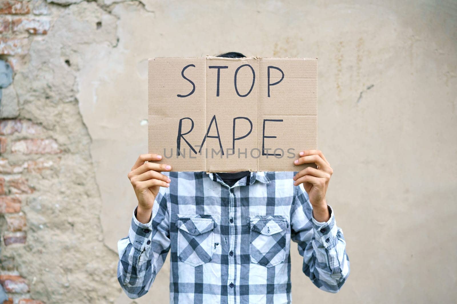 Young man holding cardboard with the inscription stop rape. Guy of Caucasian appearance against violence holds a poster with a protest at the demonstration against the background of the wall