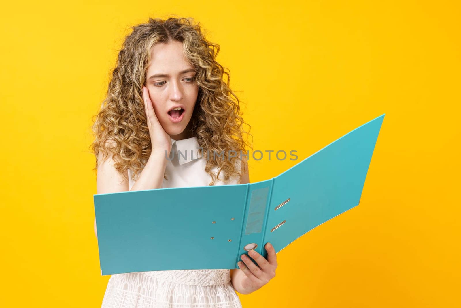 A young woman holds folders with documents in her hands. Reads and wonders. Isolated on yellow background