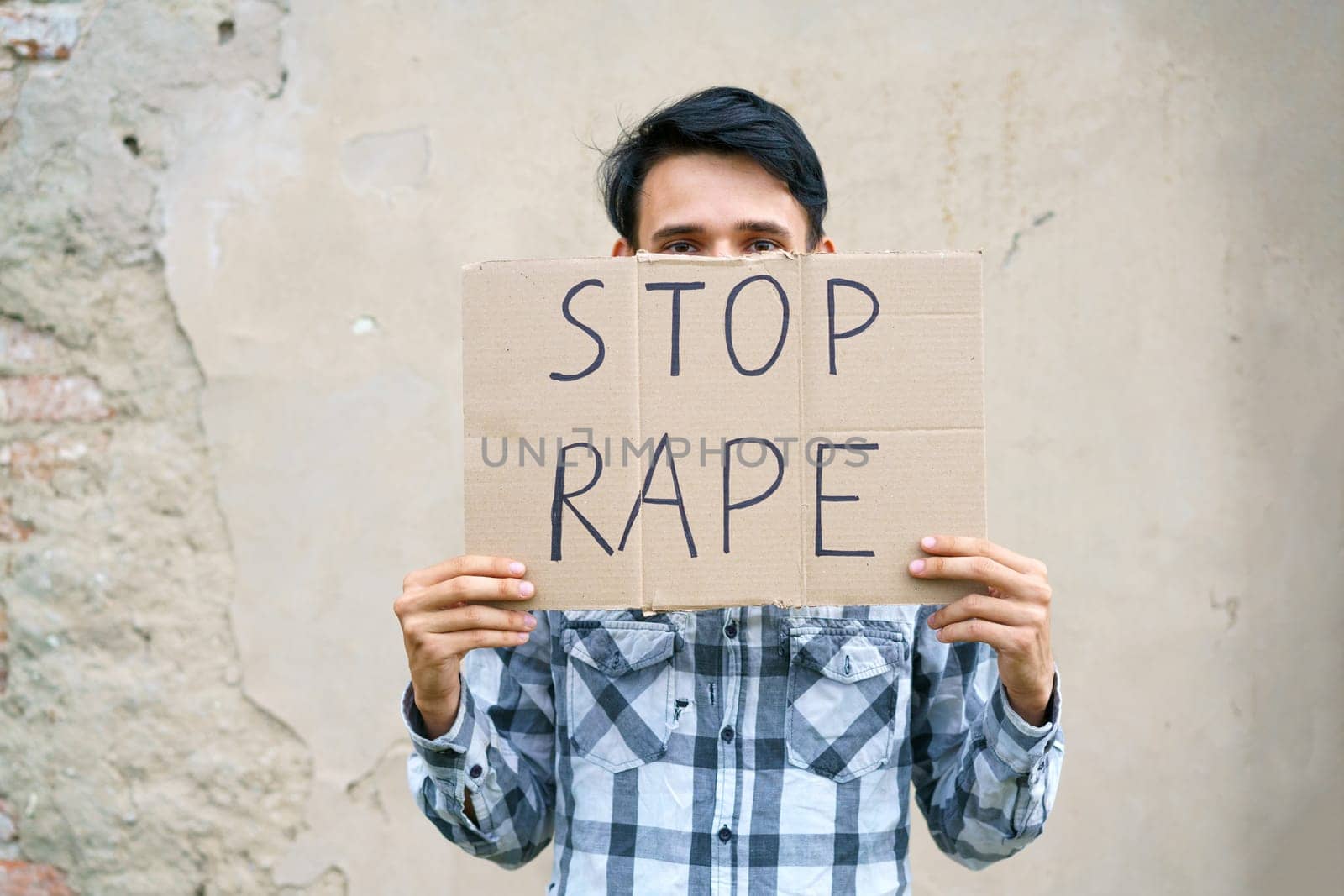 Young man holding cardboard with the inscription stop rape. Guy of Caucasian appearance against violence holds a poster with a protest at the demonstration against the background of the wall