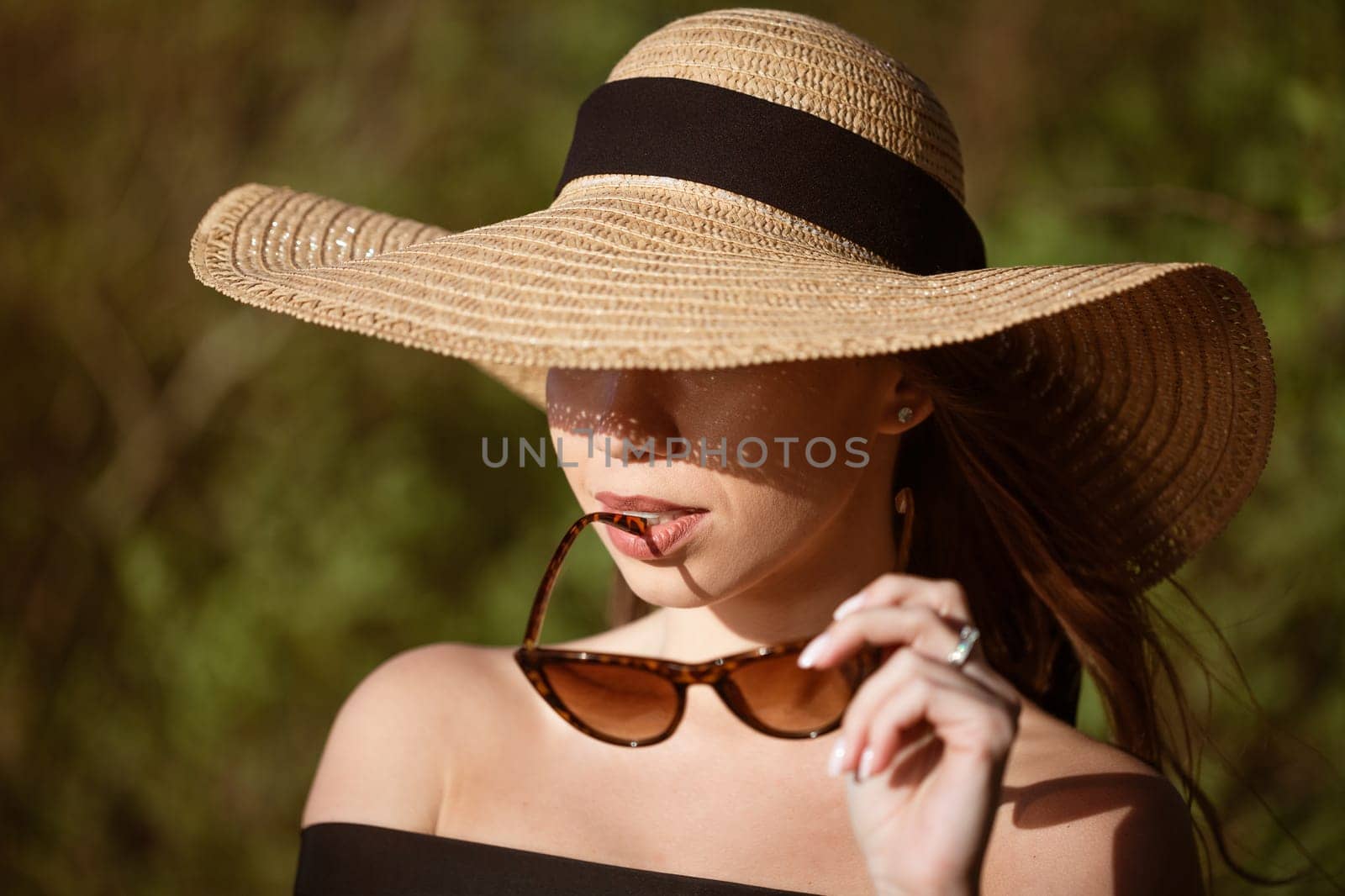 Young happy woman of Caucasian appearance in a straw hat close-up in sunglasses posing on a sunny summer day on the beach.