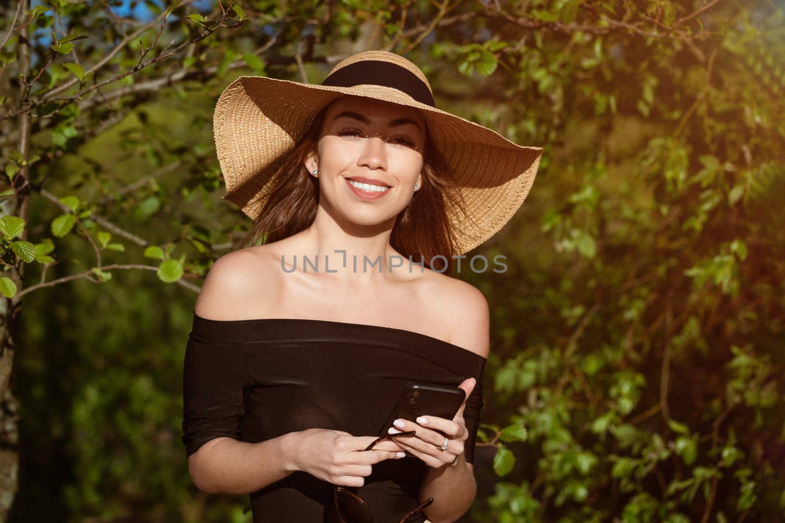 Beautiful happy woman in hat with phone in hand in summer by EkaterinaPereslavtseva