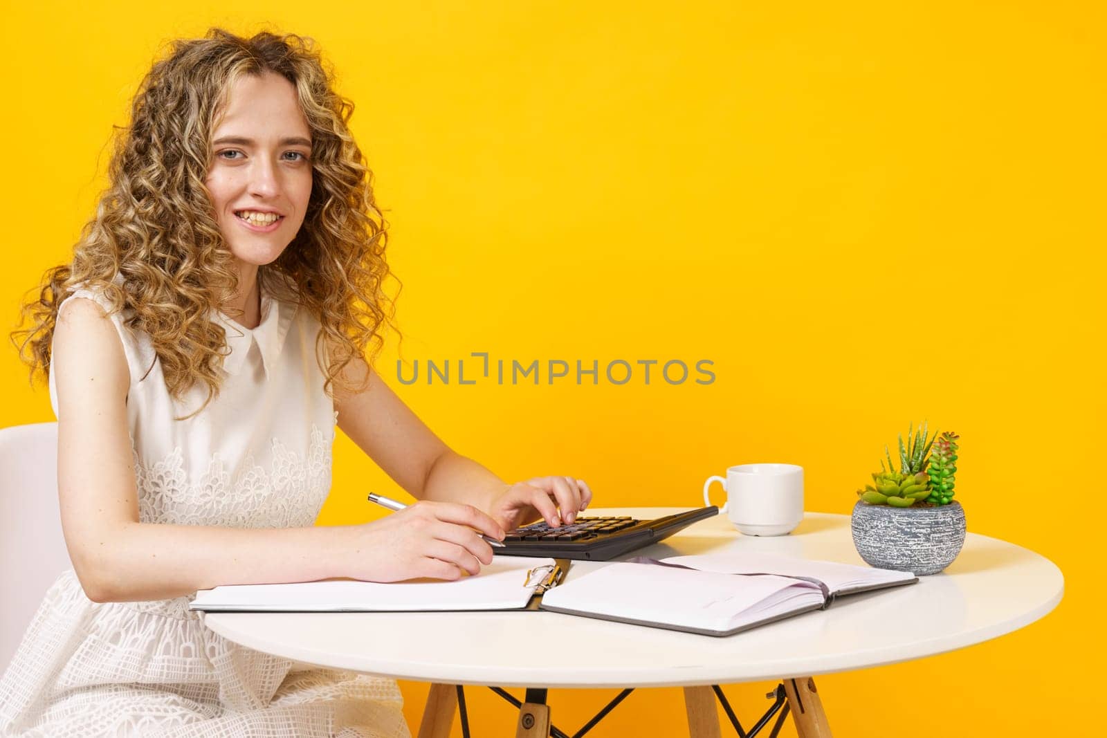 A young woman sits at a table, works with documents, considers, studies. Education. Business. Isolated on yellow background