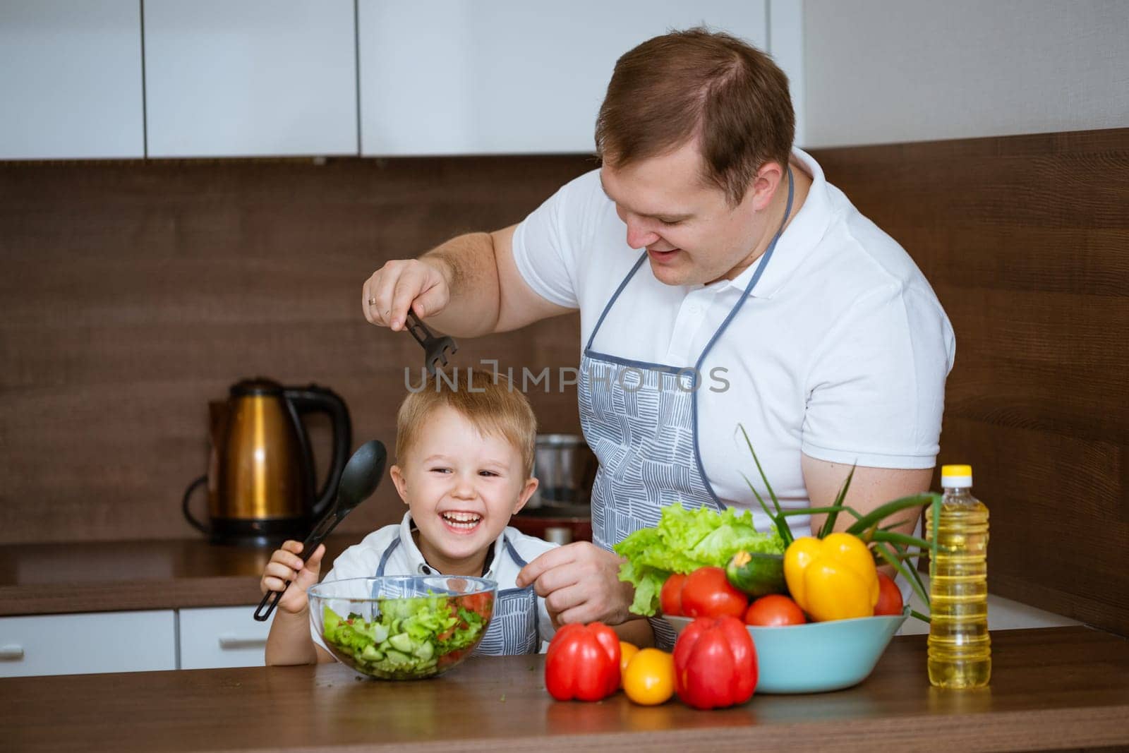 son and father prepare salad together in the kitchen by EkaterinaPereslavtseva