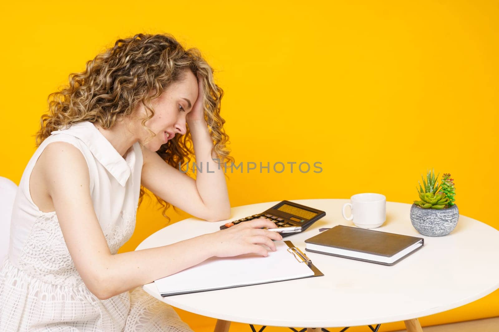 A young woman sits at a table, works with documents, considers, studies. Education. Business. Isolated on yellow background