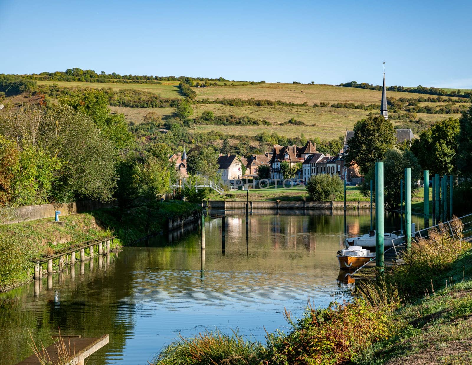 a small harbor with boats and the French village of Les andelys with the green hills in the background in summer