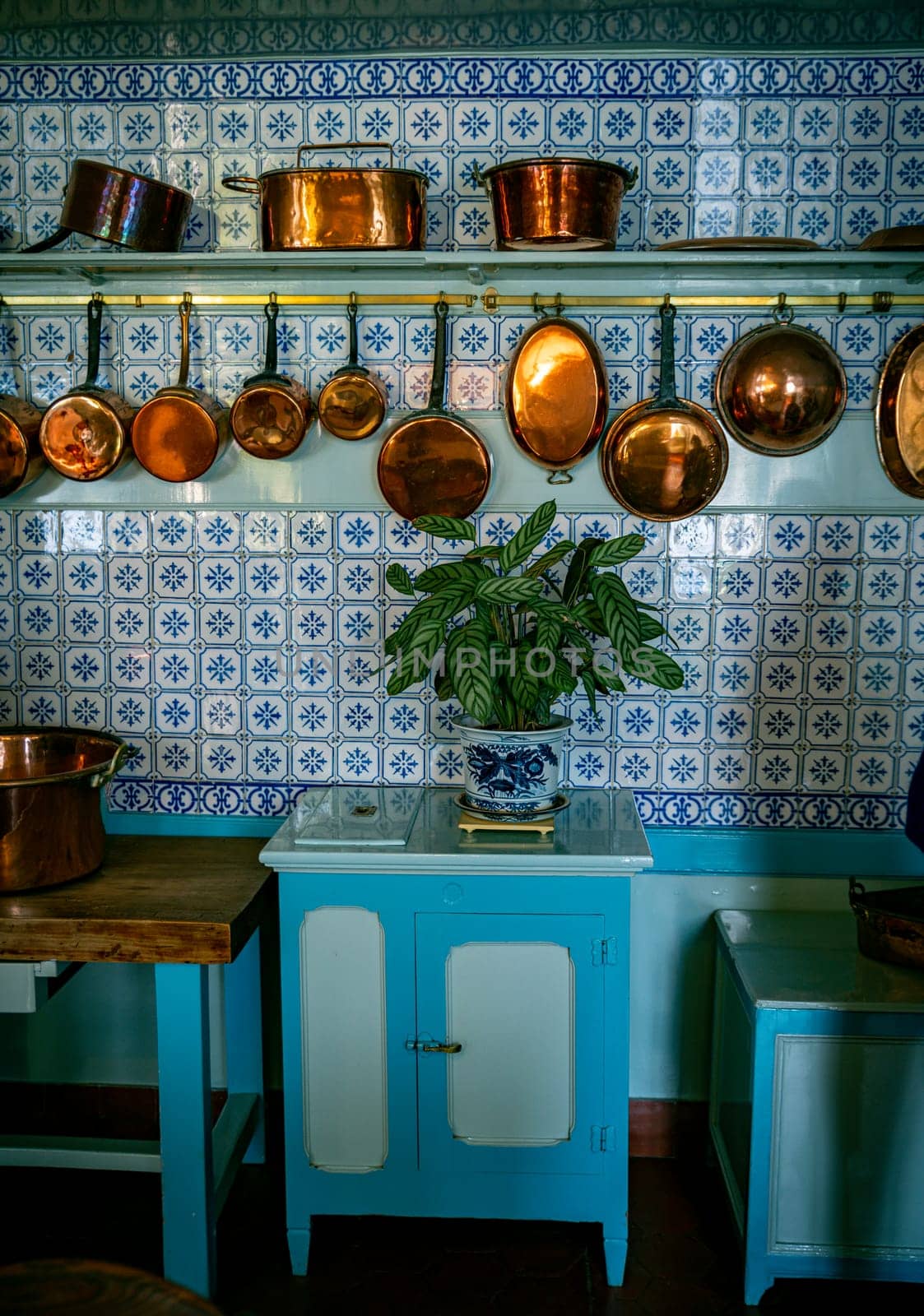 an old vintage kitchen with copper pots and pans with a blue tiled wall by compuinfoto