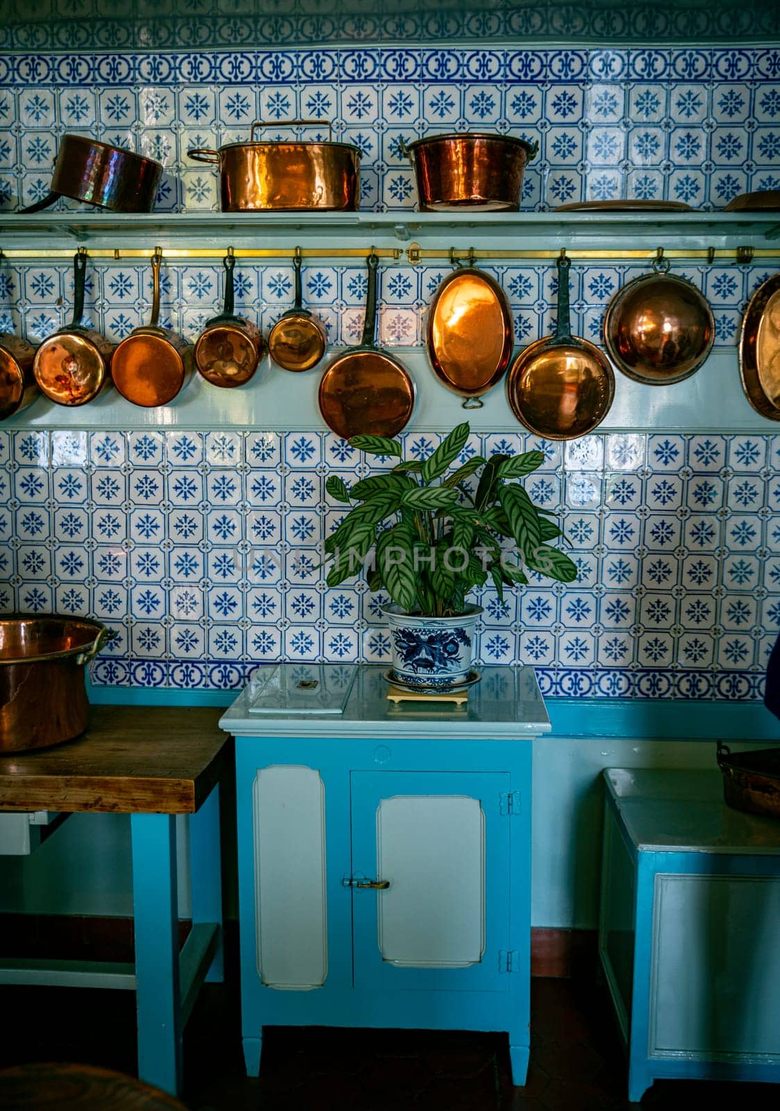 old kitchen with copper pans on the wall and blue tiles on the wall above a number of blue cupboards