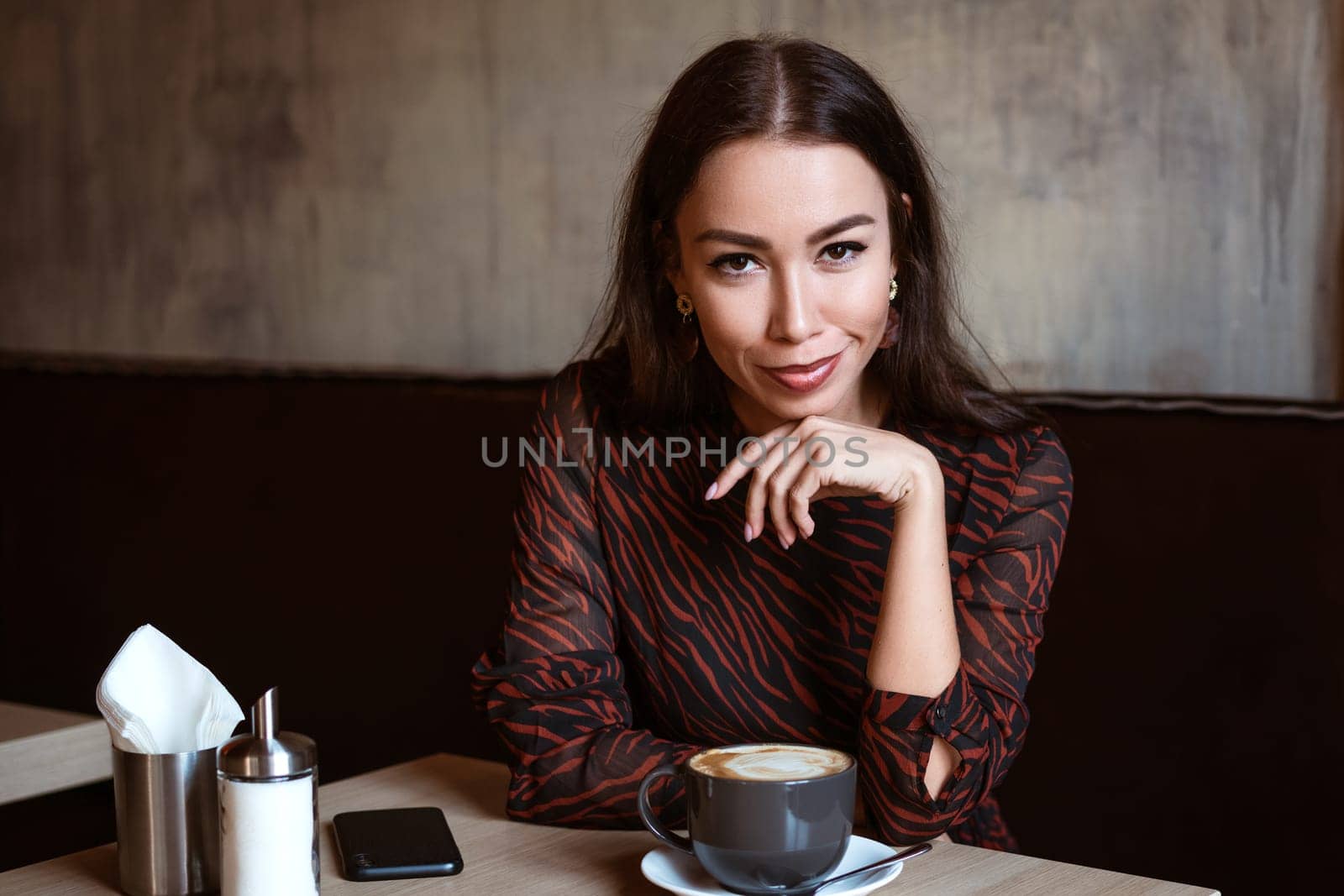 Portrait of a young woman of Caucasian appearance in a cafe with a cup of coffee. Beautiful brunette with brown eyes. Enjoying morning coffee in a cozy cafeteria