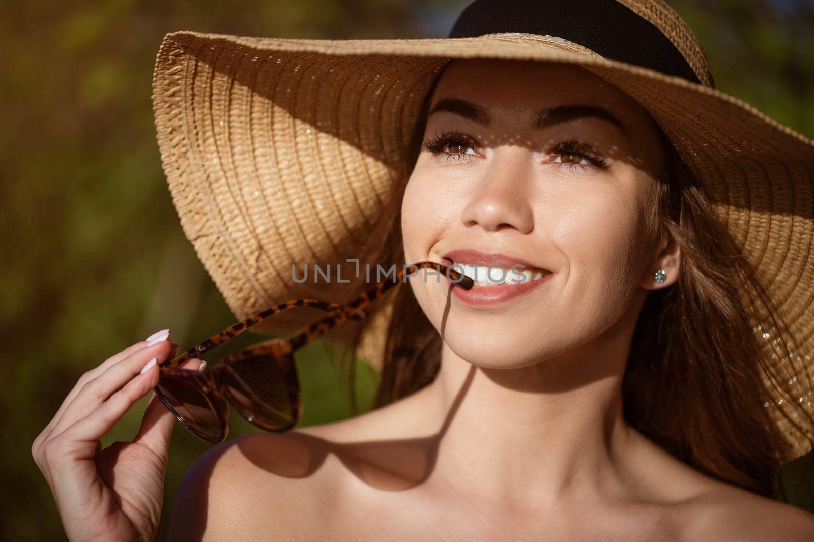 Beautiful young woman in a straw hat in black outdoors on a sunny day smiling, close-up. Happy caucasian girl in the summer on nature