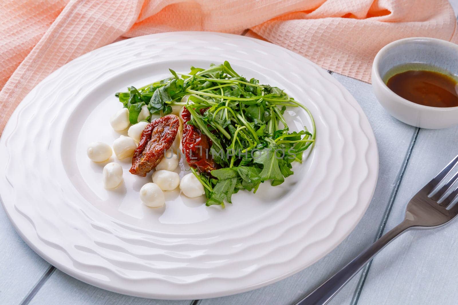 Fresh salad with arugula, mozzarella cheese, sun-dried tomato and white wood dressing