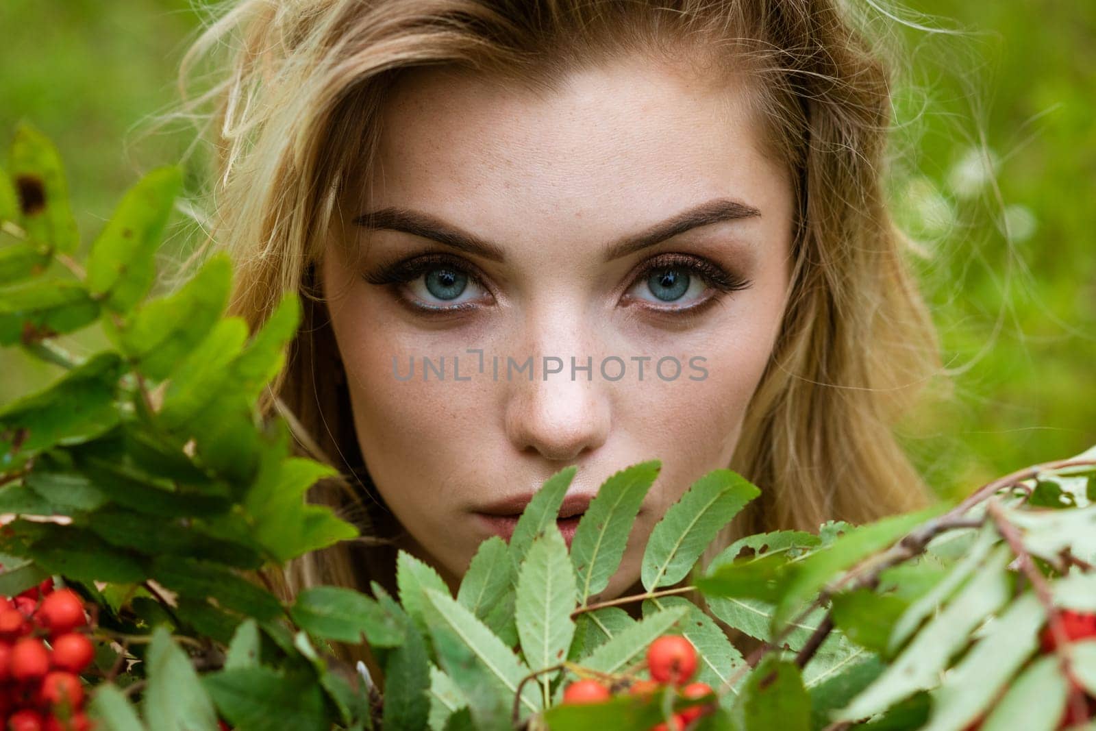 Portrait of a young beautiful blonde woman with a bouquet of rowan berries in nature close-up